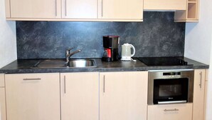Una cocina moderna con armarios de colores claros, encimera negra, pileta de acero inoxidable, cafetera y horno integrado.