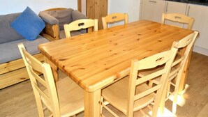 Una mesa de comedor de madera con seis sillas, un sofá gris con cojines azules, y una cocina con encimera y armarios negros.