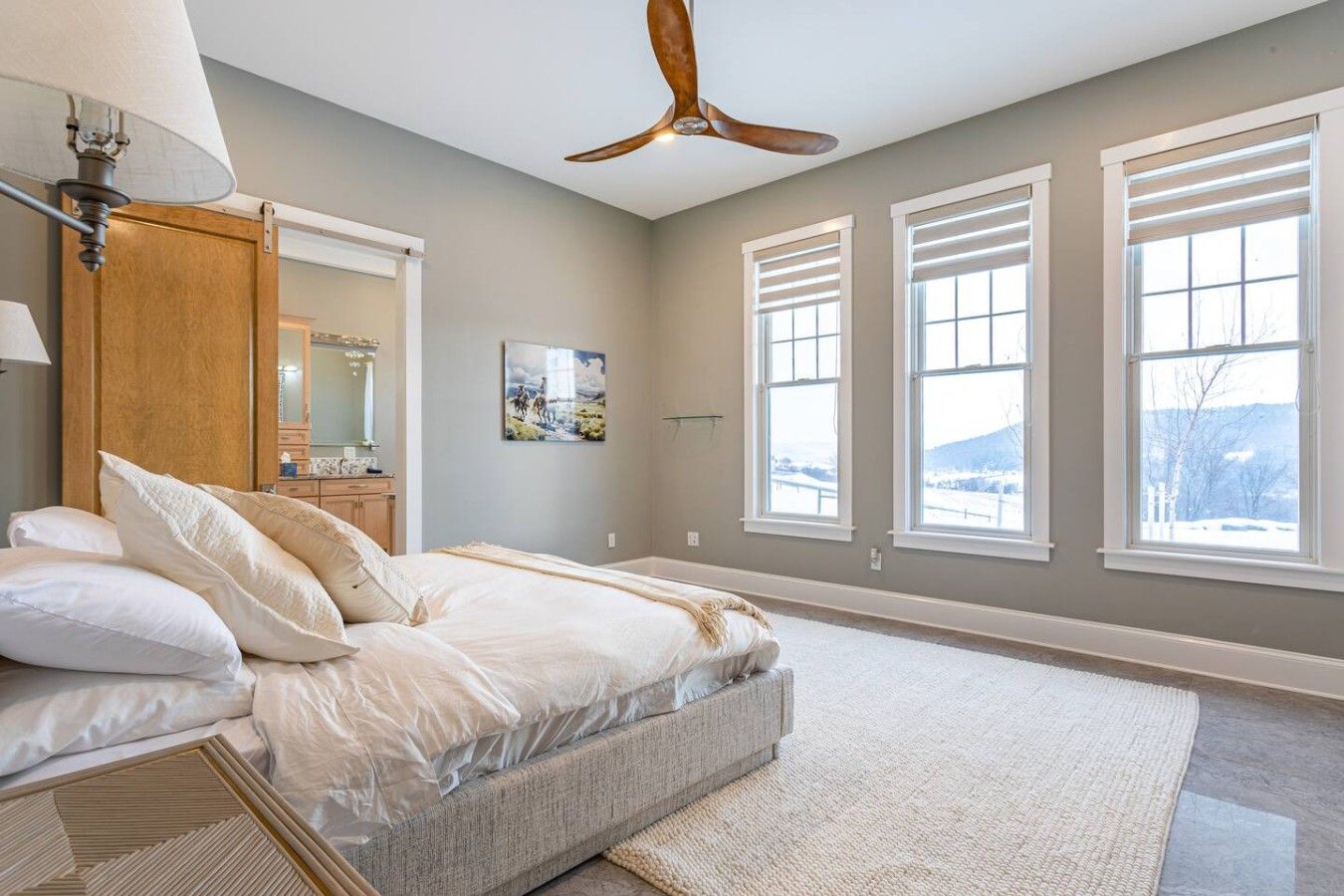 Une chambre à coucher avec un lit, un ventilateur de plafond, de grandes fenêtres et une vue sur l’extérieur.