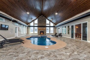 An indoor swimming pool with a stone fireplace, lounge chairs, and a high ceiling with wooden beams. - Equestrian Estate | Indoor Pool, Theater, Game Rm (Schoharie)