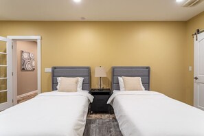 A hotel room with two beds, a nightstand, a lamp, and a door. - Equestrian Estate | Indoor Pool, Theater, Game Rm (Schoharie)