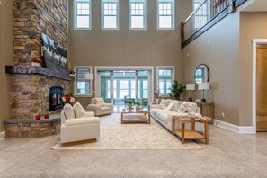 A spacious living room with a stone fireplace, multiple seating areas, and large windows. - Equestrian Estate | Indoor Pool, Theater, Game Rm (Schoharie)