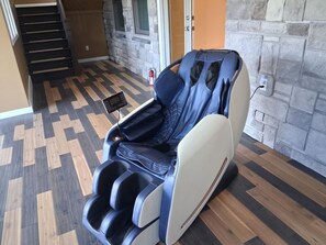A massage chair in a room with a herringbone floor pattern, a stone wall, and a door in the background. - Equestrian Estate | Indoor Pool, Theater, Game Rm (Schoharie)