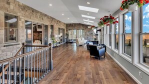 Un intérieur spacieux avec un mur en pierre, de grandes fenêtres, un plancher en bois et un escalier.