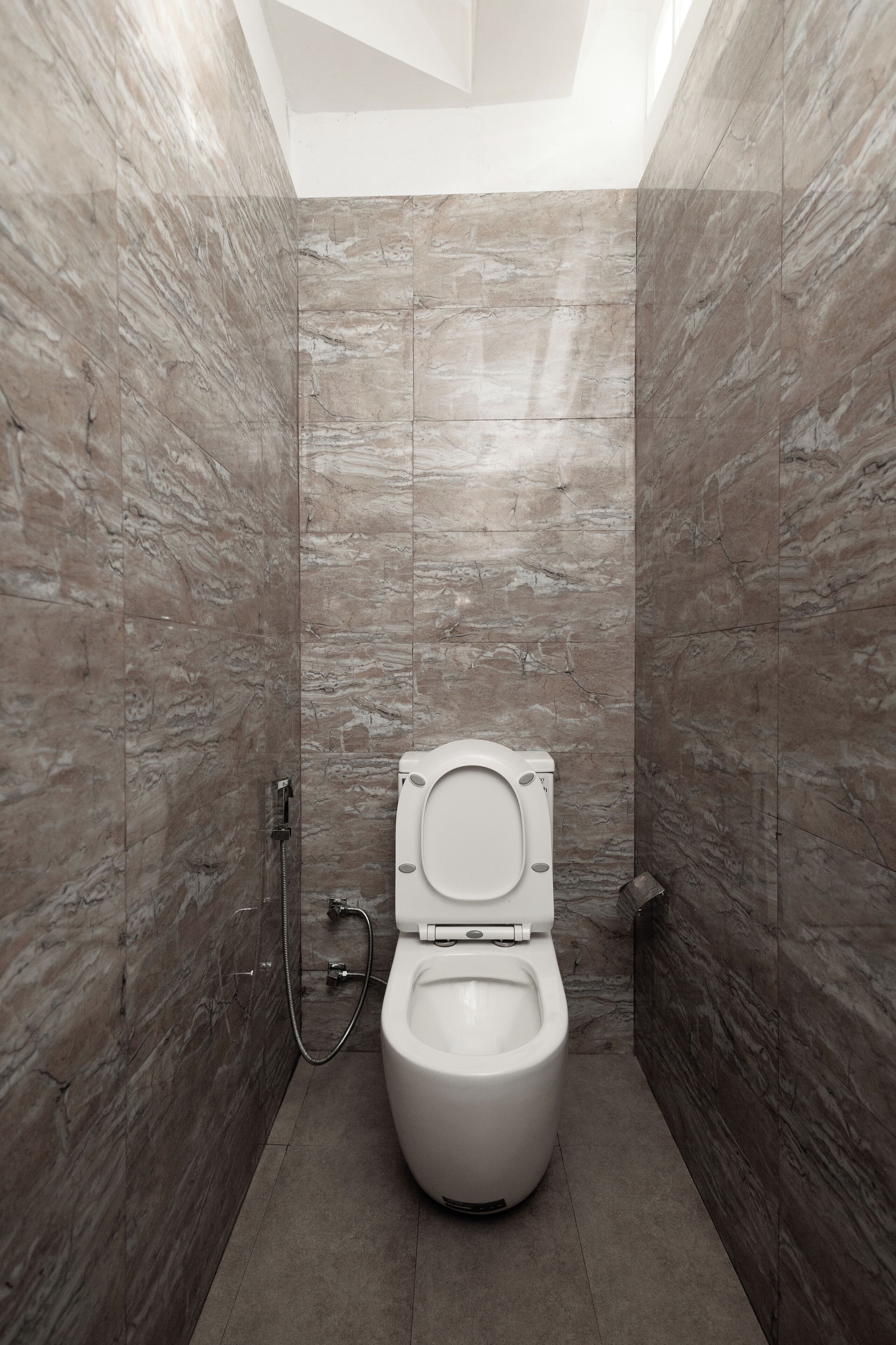 A modern bathroom with a marble wall, a toilet, and a shower.