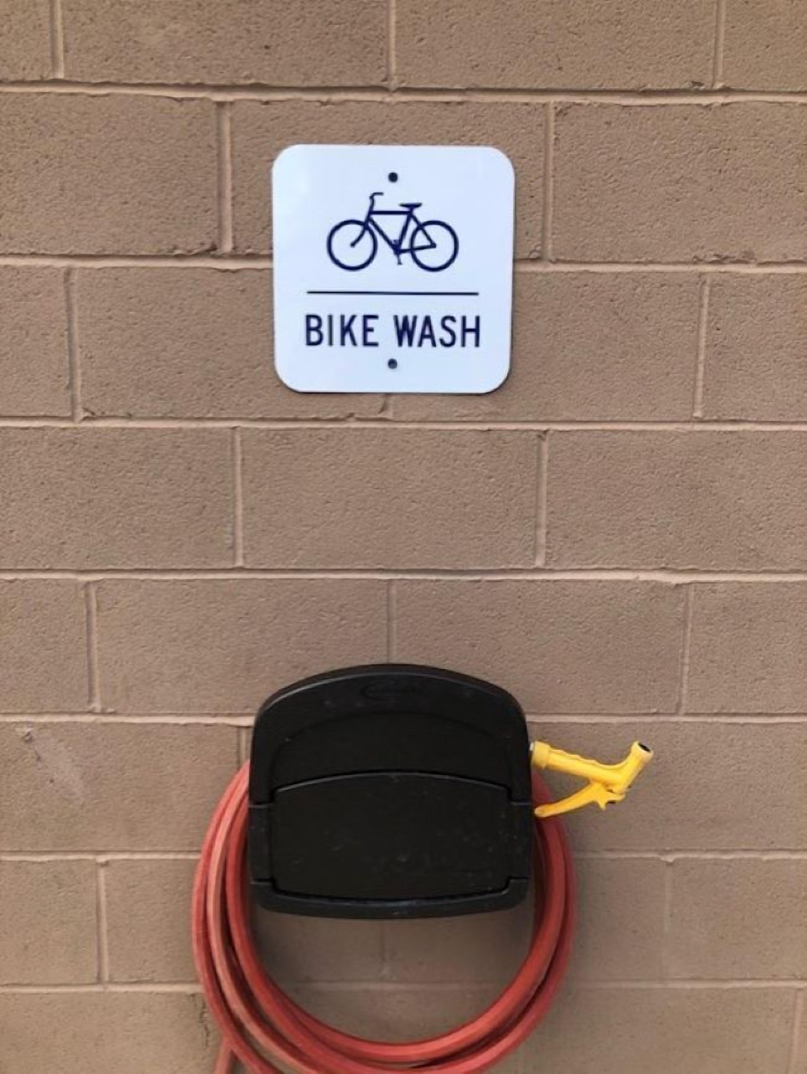 Un letrero de lavado de bicicletas y una estación de lavado con una manguera y una bomba, todo frente a un muro de ladrillo.