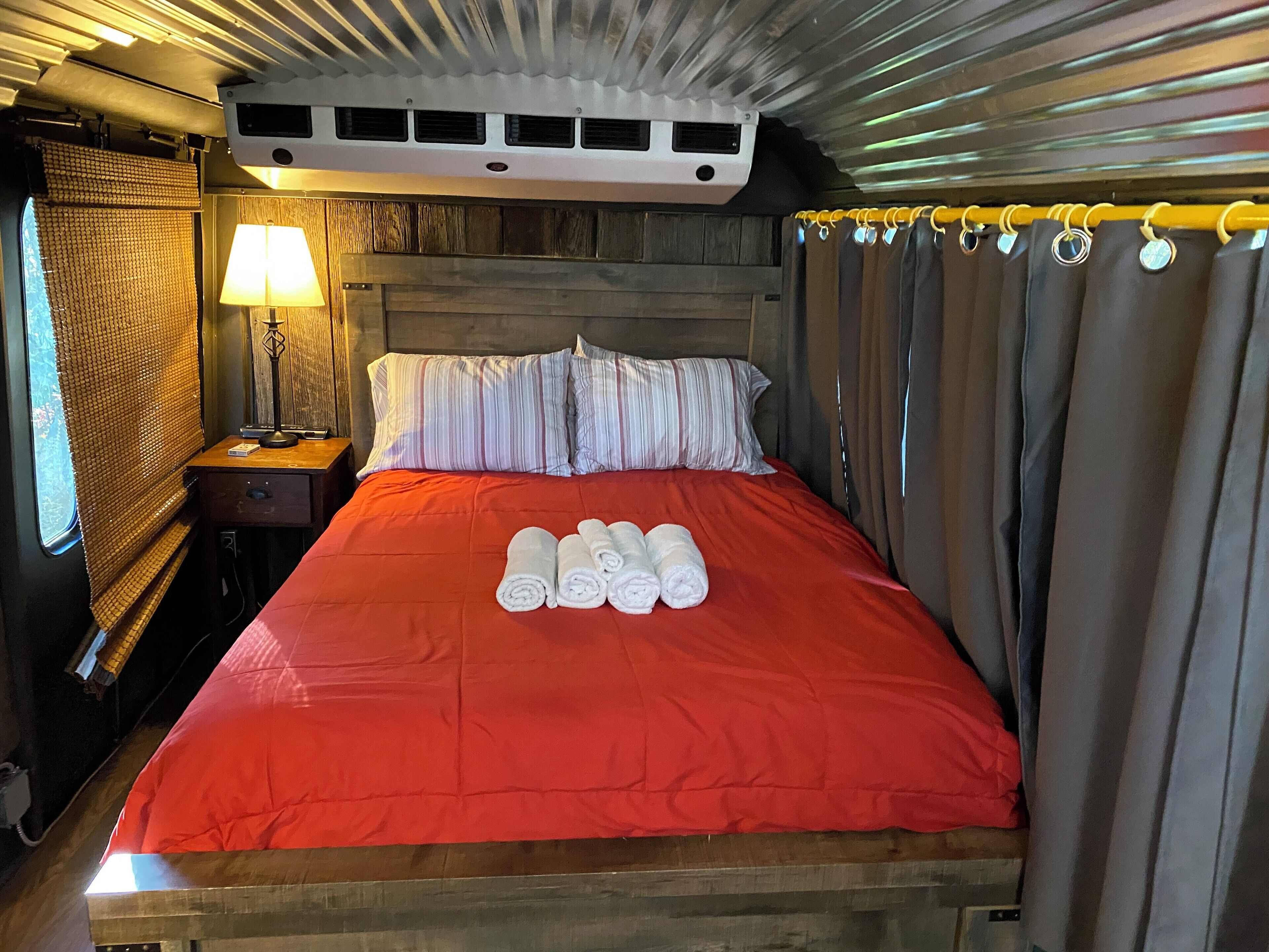 Un lit avec une couverture rouge, deux oreillers et des serviettes enroulées posées sur le lit.