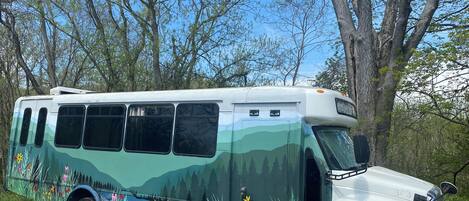 Een groene bus met kleurrijke bloemmotieven, geparkeerd in een bebost gebied.