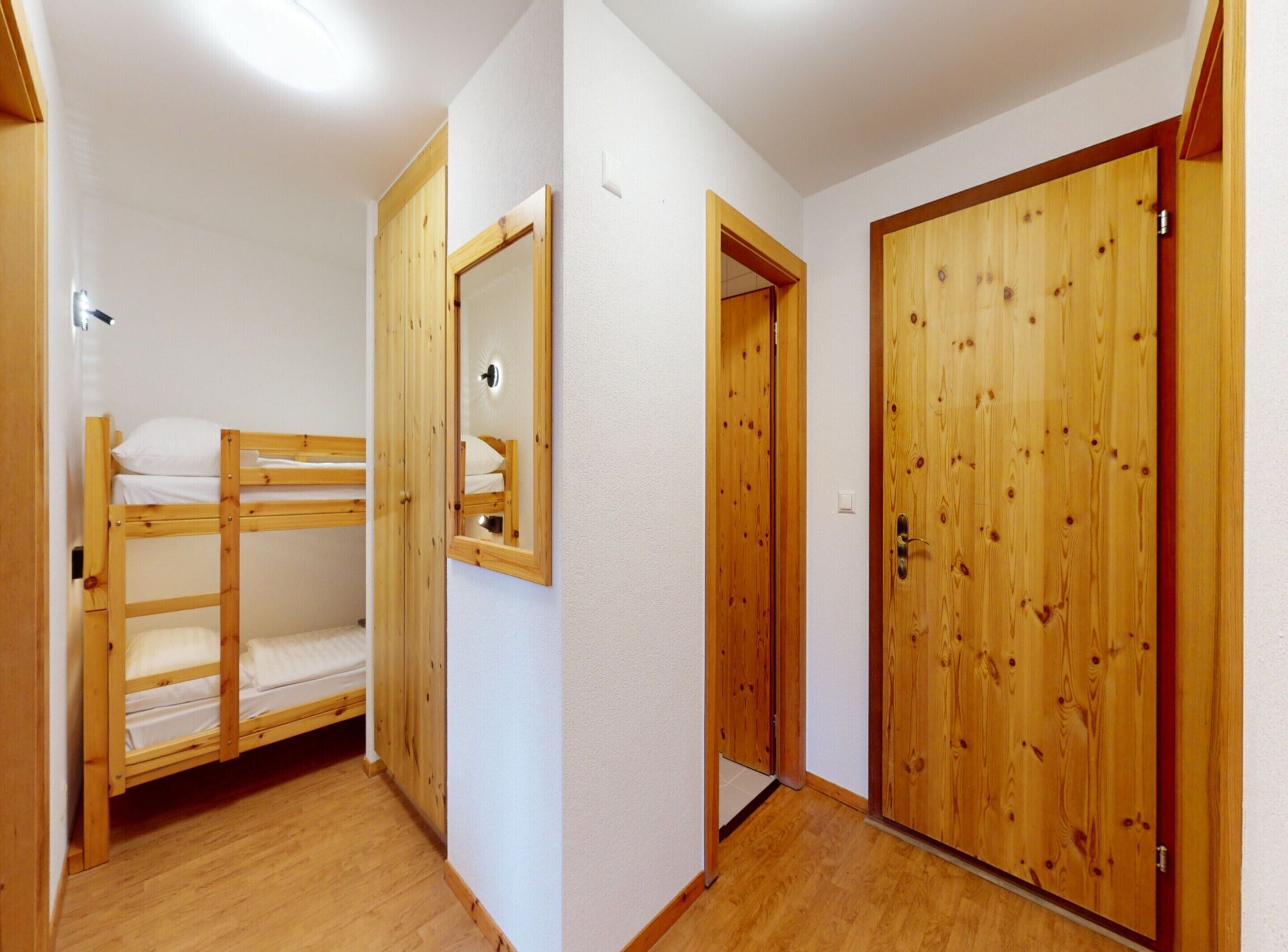 Una habitación con una cama litera, una puerta de madera y un espejo en la pared.