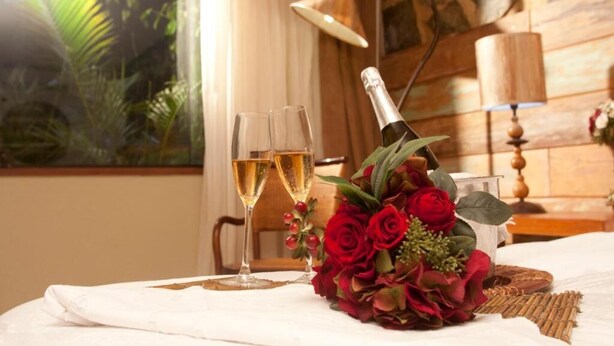 A table with a bottle of champagne, two glasses, and a bouquet of red roses. - Hotel Fazenda Parador Maritacas (Barra do Pirai)