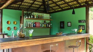 Eine Bar mit einer Holztheke, Barhocker und Regalen voller Flaschen und Gläsern.