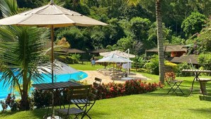 Ein Poolbereich mit Liegestühlen und Sonnenschirmen, umgeben von üppiger Vegetation und einem klaren, blauen Pool.