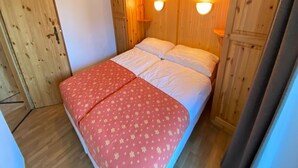A small, cozy room with wooden walls and a bed with a red patterned bedspread. There are two wall-mounted lights above the bed. - Apartment in the Heart of Valley (Nendaz)