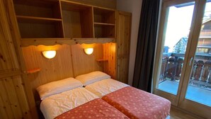 A double bed with a red floral bedspread and white pillows in a wooden room with built-in shelves and two wall-mounted lights. - Apartment in the Heart of Valley (Nendaz)
