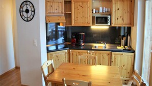 A kitchen with wooden cabinets, a microwave, a coffee maker, and a dining table with chairs. - Apartment in the Heart of Valley (Nendaz)