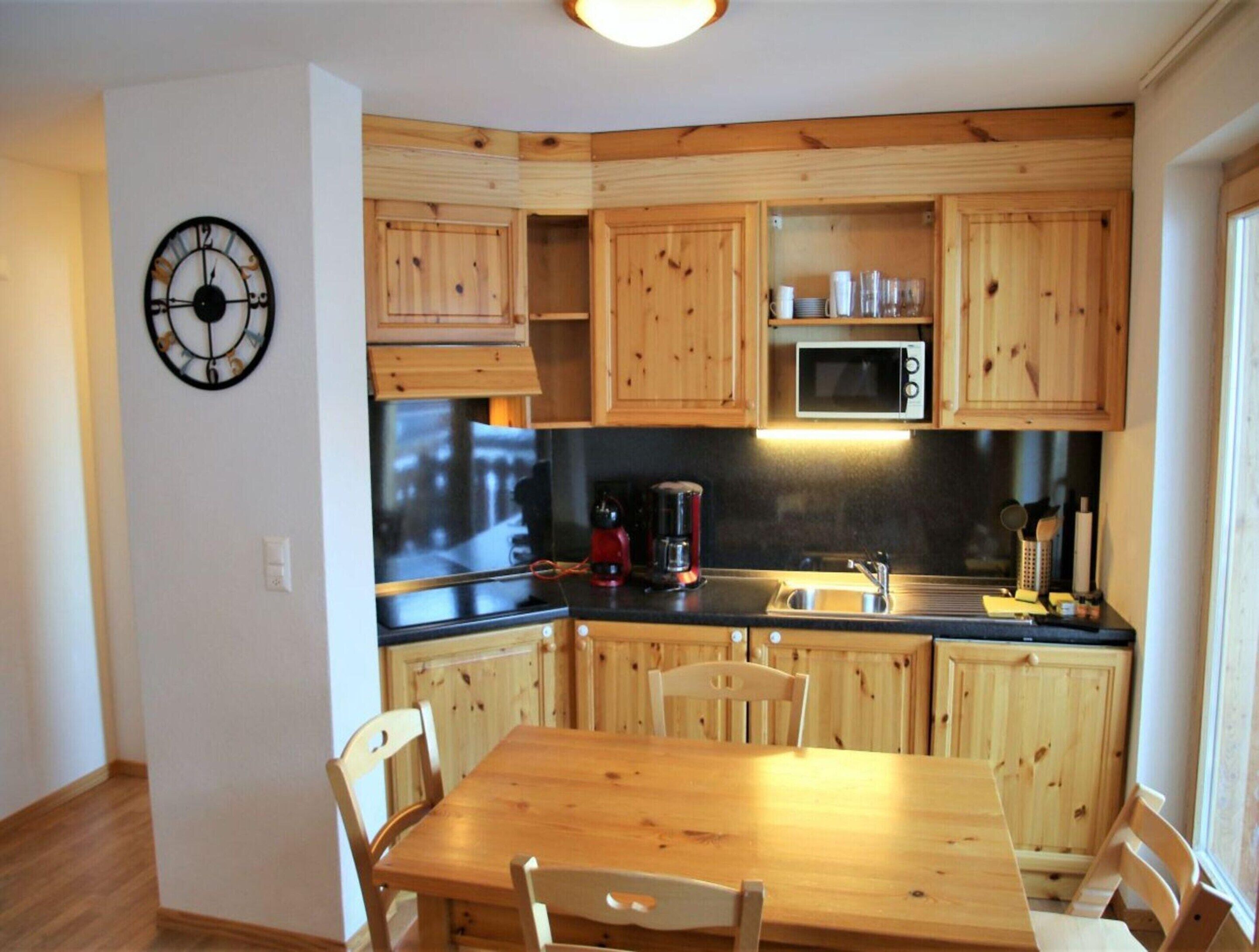 A compact kitchen with wooden cabinets, a microwave, a coffee maker, and a dining table with chairs.