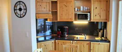 A compact kitchen with wooden cabinets, a microwave, a coffee maker, and a dining table with chairs.