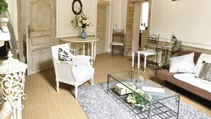 Un salon avec un canapé blanc, un fauteuil blanc, une petite table sur laquelle est posé un vase de fleurs et un miroir accroché au mur.