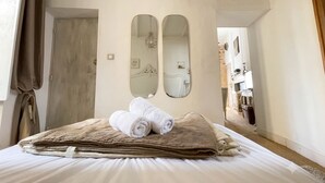 Une chambre d’hôtel avec un lit, deux miroirs, une porte et un couloir menant à une autre pièce.