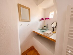 Une salle de bain avec un lavabo en verre, un miroir, une étagère avec des serviettes et une orchidée.