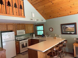 A kitchen with wooden cabinets, a refrigerator, a microwave, a stove, and a large island with bar stools.