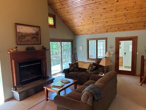 A living room with a fireplace, a couch, a coffee table, and a view of the outdoors through large windows.