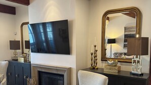 Sala de estar com lareira, televisão fixada na parede, espelho grande e armário escuro.