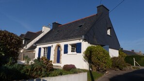 A traditional house with a steeply pitched roof, a prominent chimney, and a small front garden with various plants. - Les Courlis, holiday home near the beaches (Erdeven)