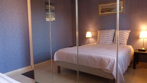 A bedroom with a bed, two bedside lamps, a nightstand, a mirror, and a framed picture on the wall.