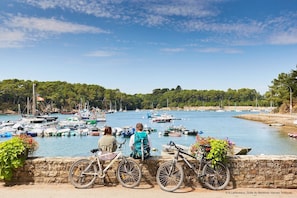 Vista costeira com barcos atracados em um porto, um muro de pedra e bicicletas estacionadas em frente.