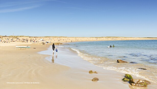 A beach with people walking, a boat, and calm water.