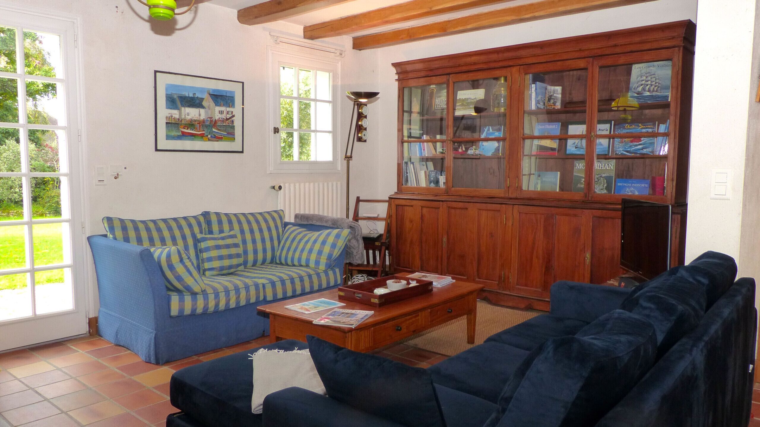 Un salón con un sofá azul a rayas, un mueble de madera con puertas de cristal y un cuadro enmarcado en la pared.