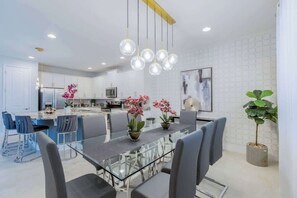 Una cucina moderna con mobili bianchi, un'isola centrale e un'area pranzo con tavolo e sedie in vetro.
