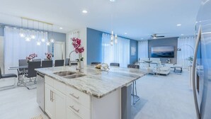 A modern kitchen with a marble countertop, a dining area with a table and chairs, and a living room with a sofa and a TV. - Gorgeous 5BR at Encore Resort next to Disney 7710 (Kissimmee)