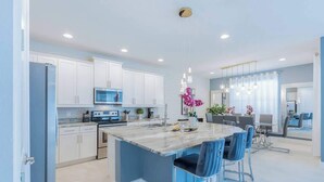 A modern kitchen with white cabinets, a central island with bar stools, and pendant lighting. - Gorgeous 5BR at Encore Resort next to Disney 7710 (Kissimmee)