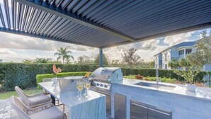 An outdoor kitchen with a grill, bar seating, and a pergola. - Gorgeous 5BR at Encore Resort next to Disney 7710 (Kissimmee)