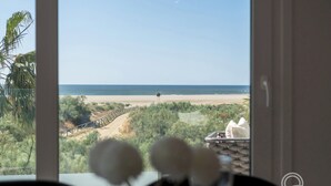 Une vue depuis une chambre dont la fenêtre donne sur une plage, un pont en bois et quelques espaces verts.