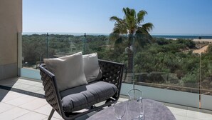 Un balcon avec vue sur la plage, un palmier et une table avec deux verres.