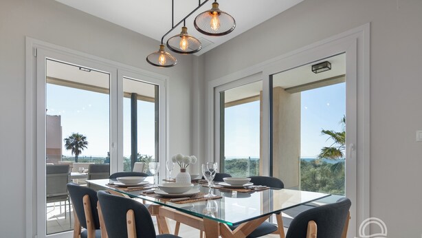 Un espace repas moderne avec une table en verre, des chaises foncées et des luminaires suspendus.