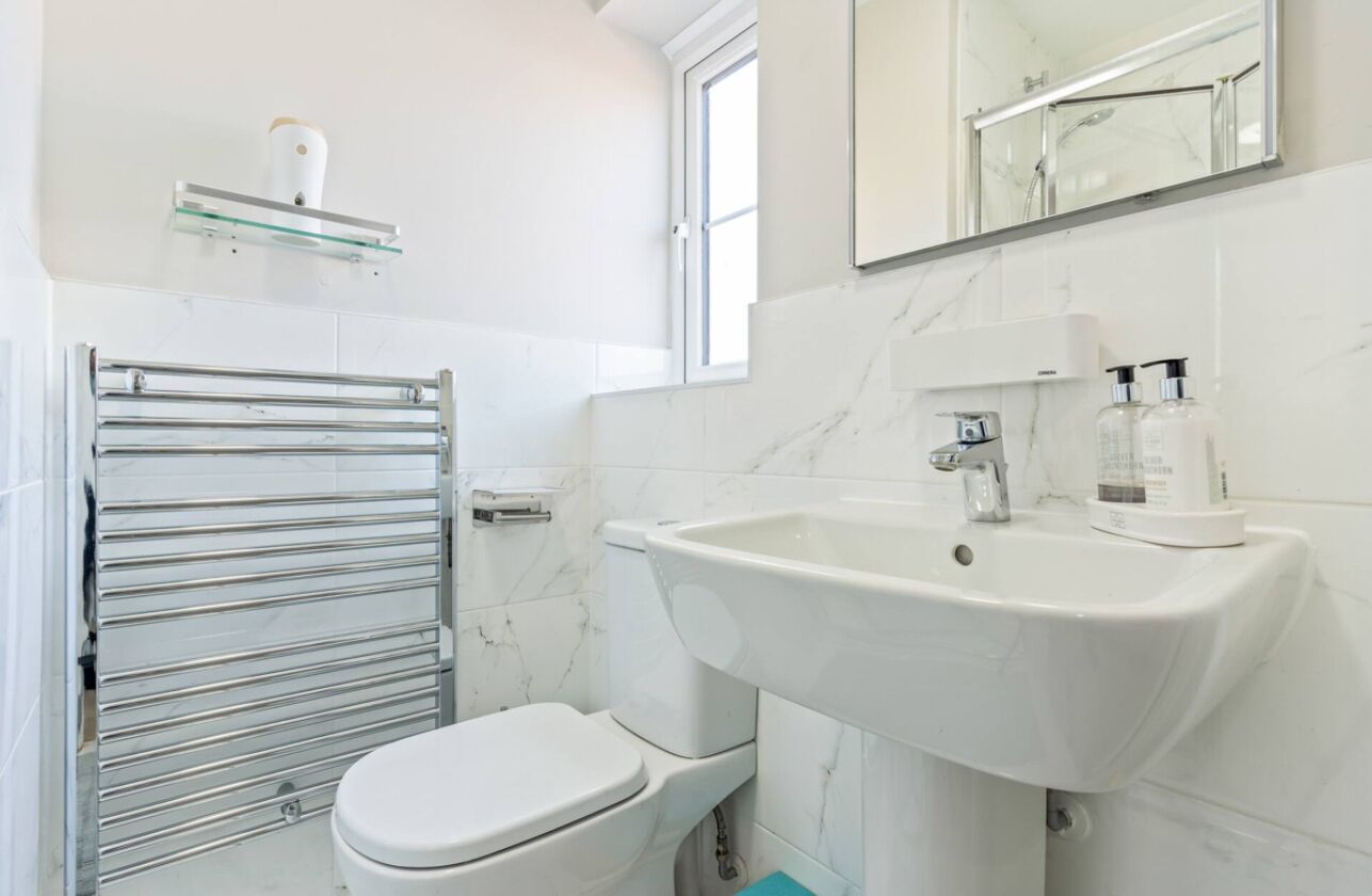 A modern bathroom with a white toilet, a glass shelf with toiletries, a white sink, and a mirror above the sink.