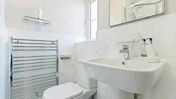 A modern bathroom with a white toilet, a glass shelf with toiletries, a white sink, and a mirror above the sink.