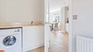 Uma cozinha moderna com armários brancos, máquina de lavar embutida e uma área de refeições com mesa e cadeiras.