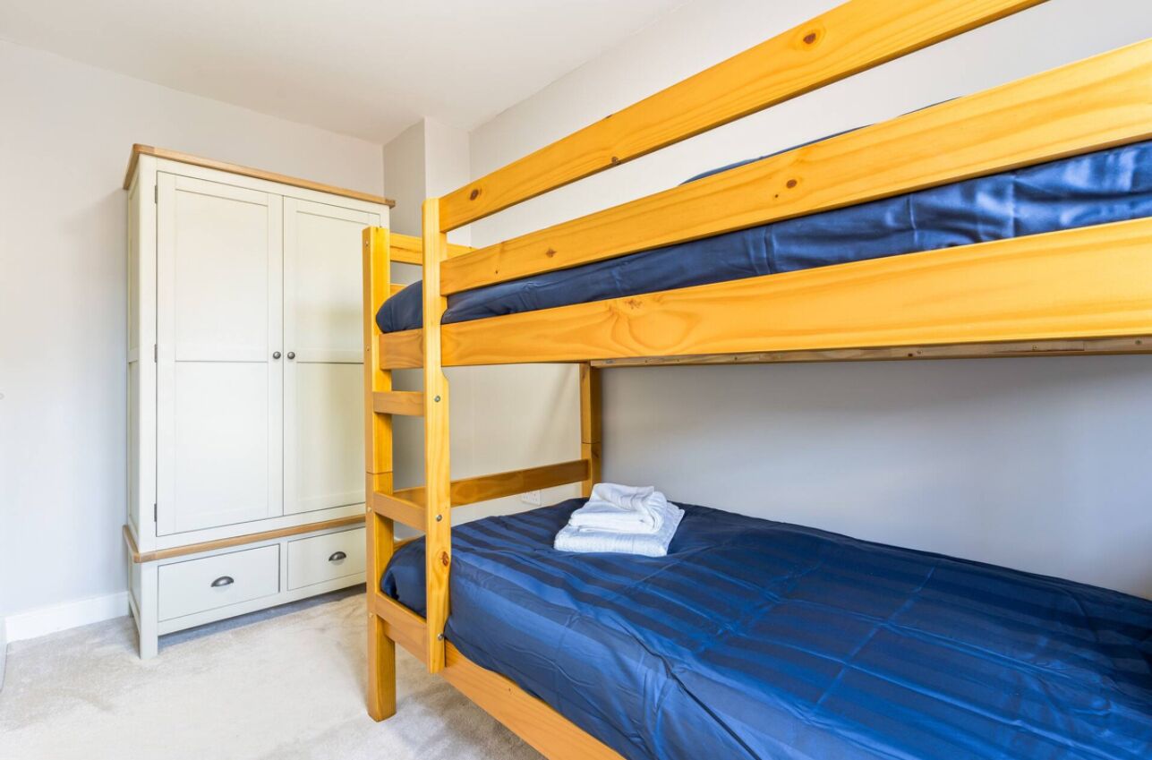 A bunk bed with a blue mattress and a wooden wardrobe with two drawers.