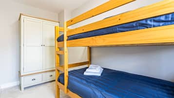 A bunk bed with a blue mattress and a wooden wardrobe with two drawers.