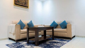 A living room with a beige sofa, blue cushions, a dark wooden coffee table, and a patterned blue rug. - Sweet Alnozha Serviced Apartments (Jeddah)
