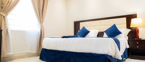 A hotel room with a large bed, a nightstand with a lamp, and a window with curtains.