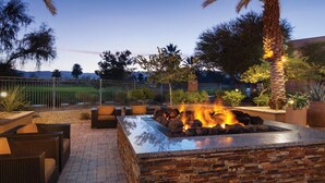 An outdoor patio with a stone fire feature, wicker furniture, and a view of the surrounding landscape. - LUXURIOUS MARRIOTT VACATION RESORT, MINUTES FROM FESTIVAL GROUNDS (Palm Desert)
