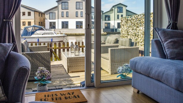 Un salon moderne doté d’une grande porte-fenêtre coulissante donnant sur un balcon avec vue sur une marina et des immeubles.
