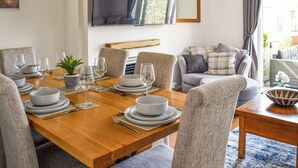 Un coin repas avec une table en bois, dressée pour quatre personnes, entourée de chaises recouvertes d’un tissu gris.