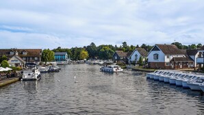 Un canal bordé de part et d’autre par des bateaux à quai, entouré de maisons et de verdure.